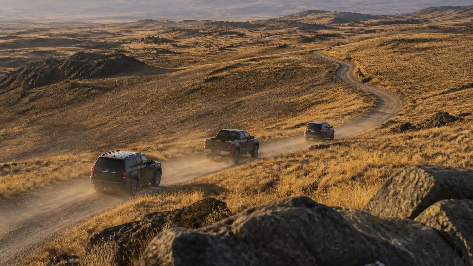 Several different 4WD body styles driving a dirt road at golden hour