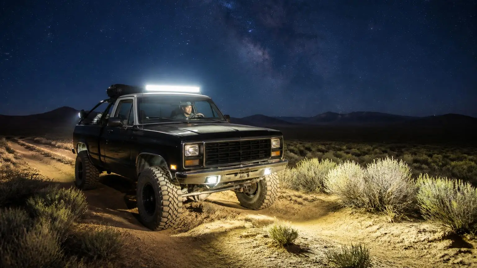 Pickup with light bar and bed rack on a night desert trail