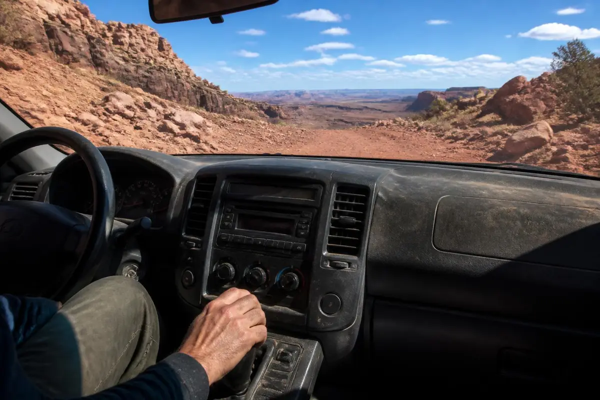 Driver's hand on the gear selector of a mid-size pickup on a rocky climb