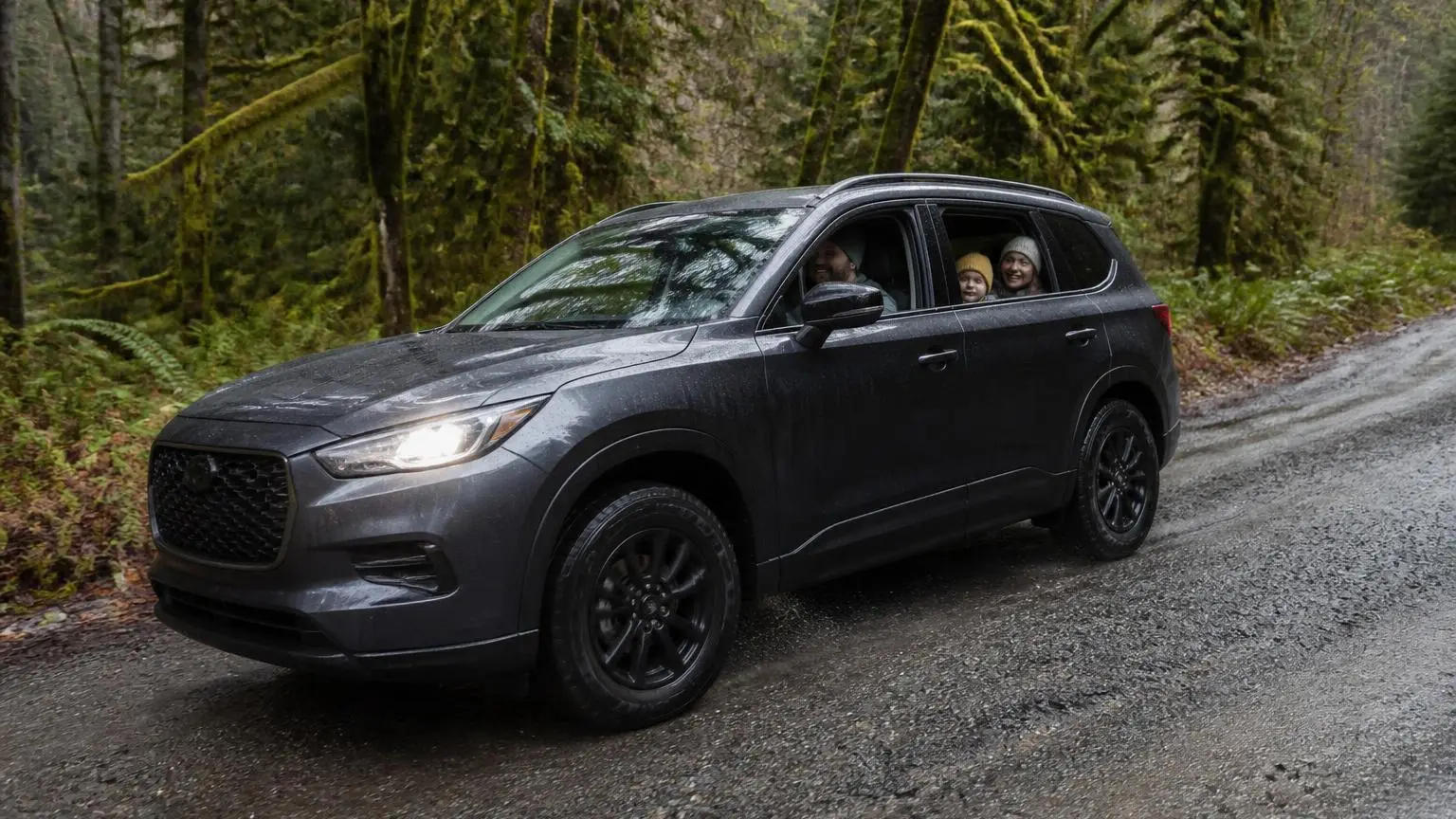 Mid-size unibody SUV driving a wet forest gravel road