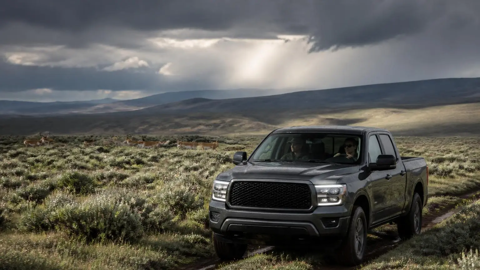 Full-size pickup crossing a sagebrush plateau under storm clouds