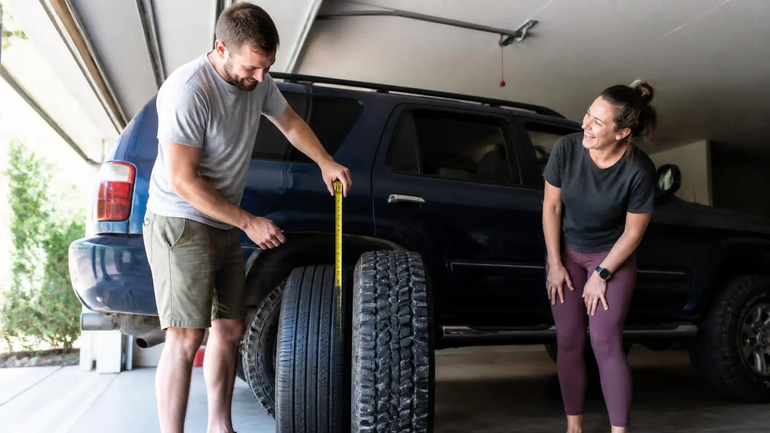 New larger tire beside a stock tire in a garage