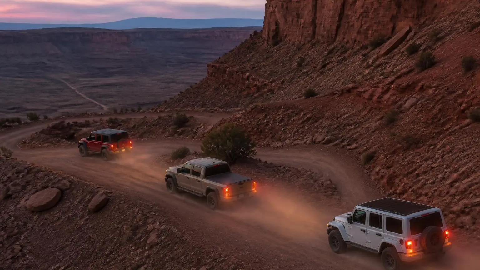Convoy of off-roaders on a dusty trail with rear lights glowing