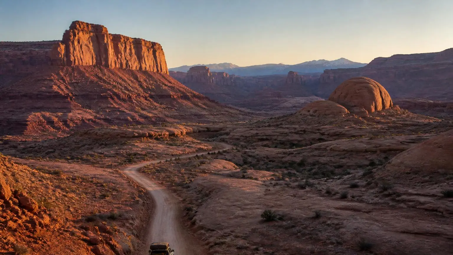 Illustrative: pickup driving a red rock desert route at sunrise