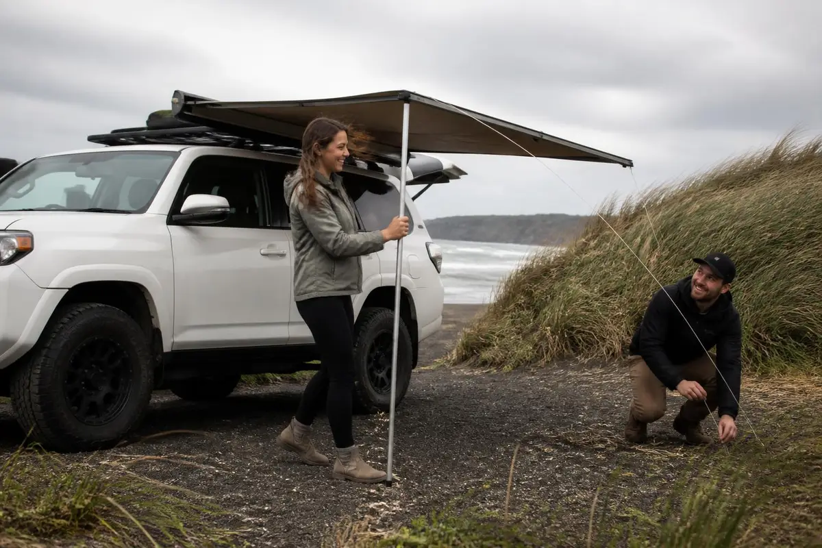 Couple deploying a side awning on an SUV in a breeze
