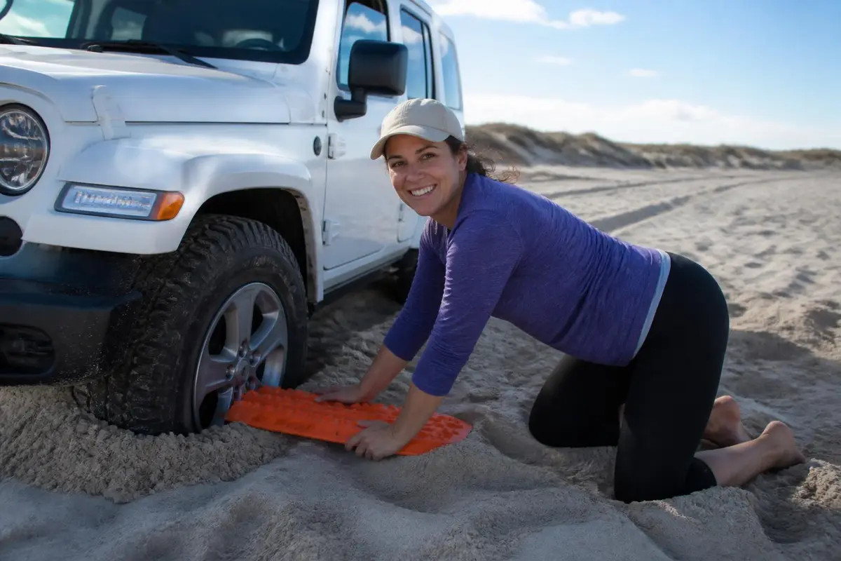 Woman placing a traction board in front of a sand-bogged tire