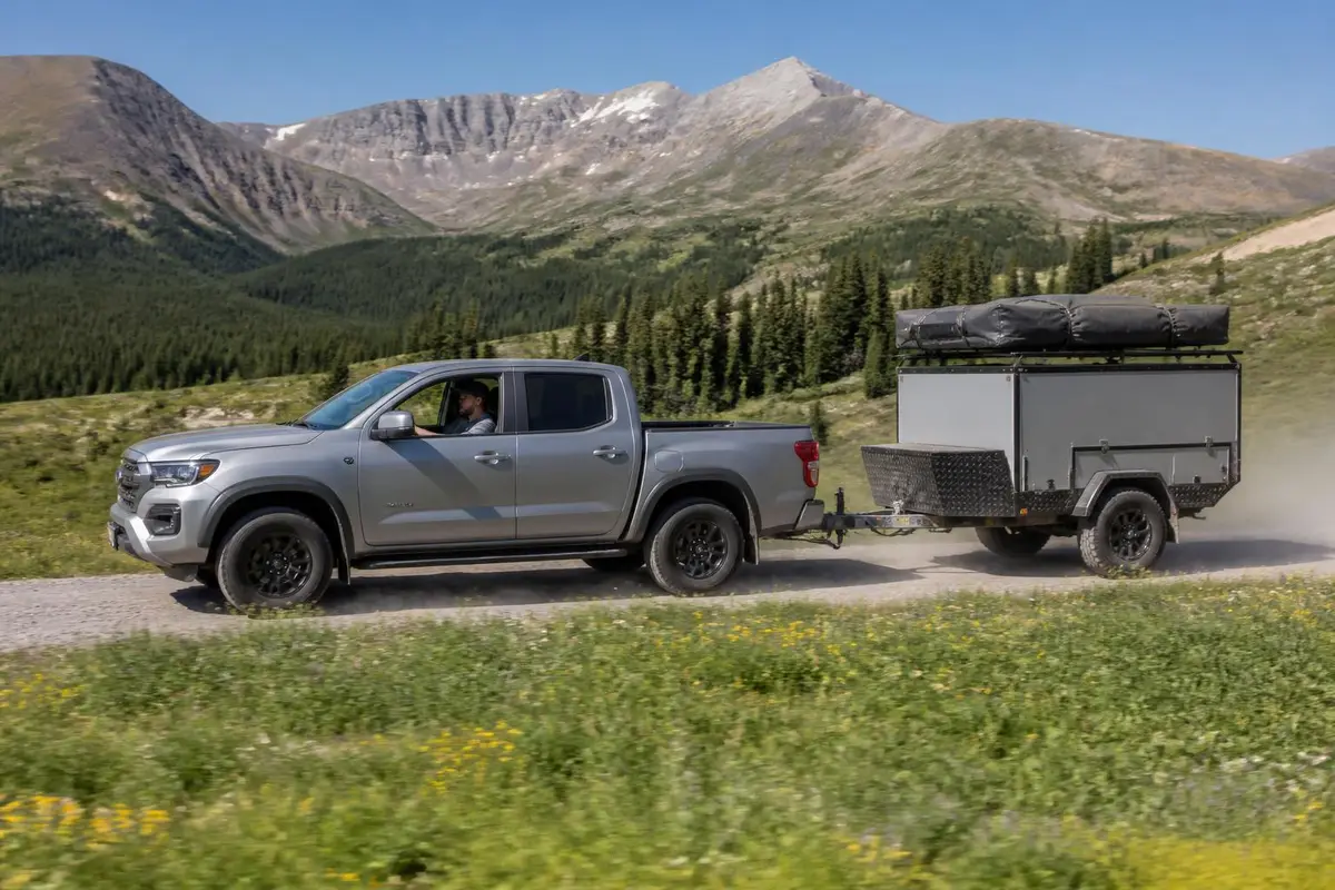 Pickup towing an overland trailer with a folded tent on a dirt road