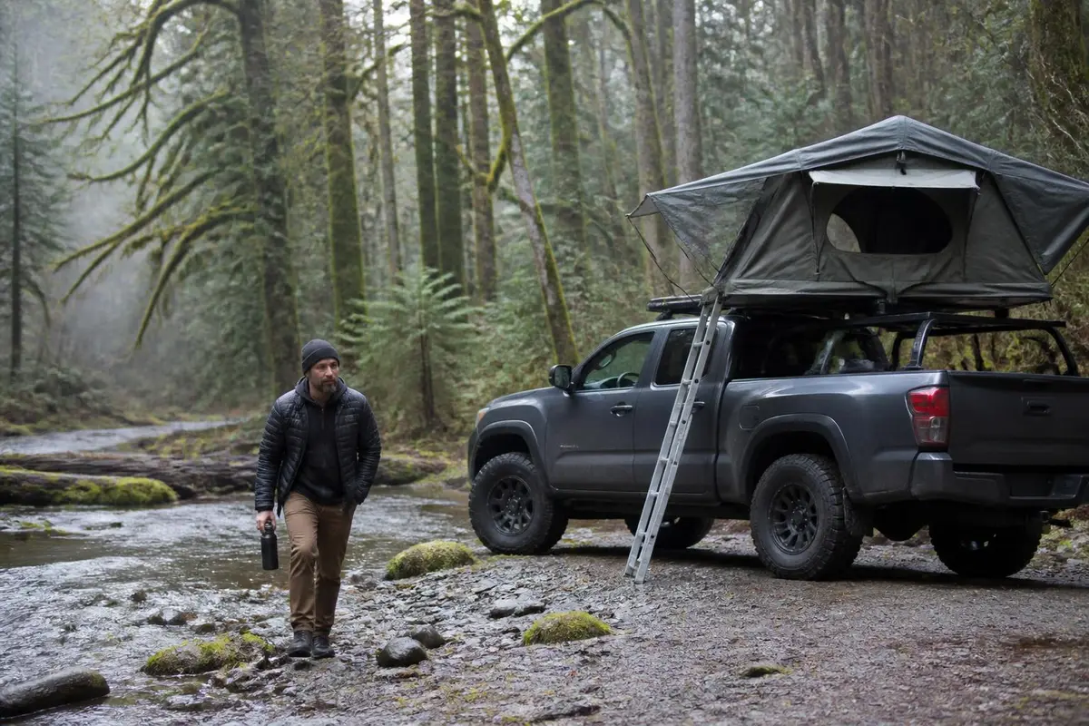 Soft-shell rooftop tent unfolded beside a forest trail