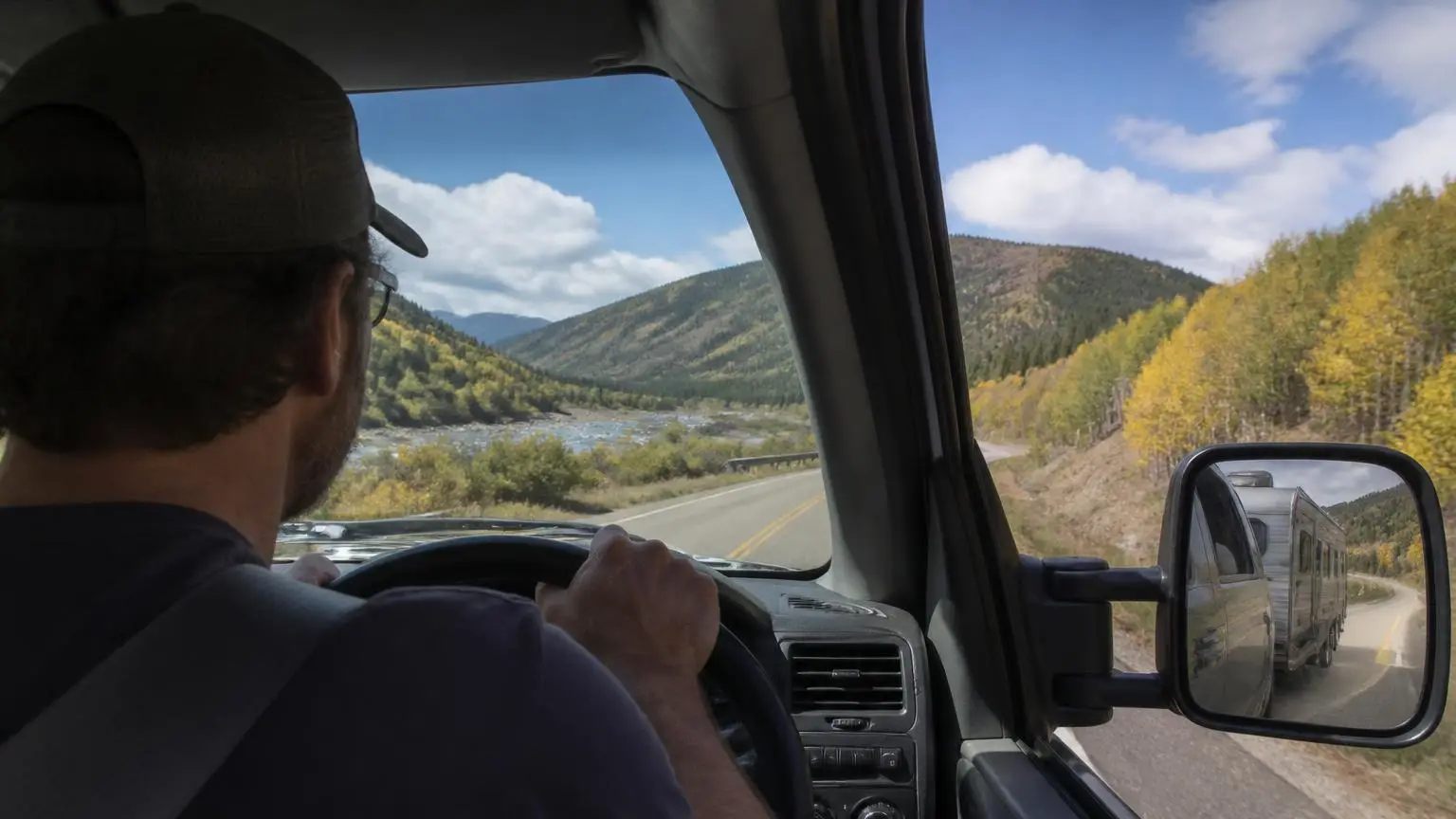 Driver's view of a towing mirror showing a trailer on a mountain road