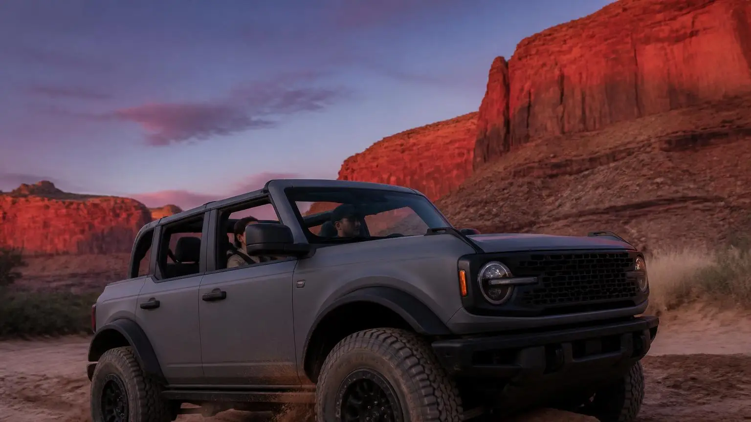 Four-door off-roader crossing a sandy wash at dusk