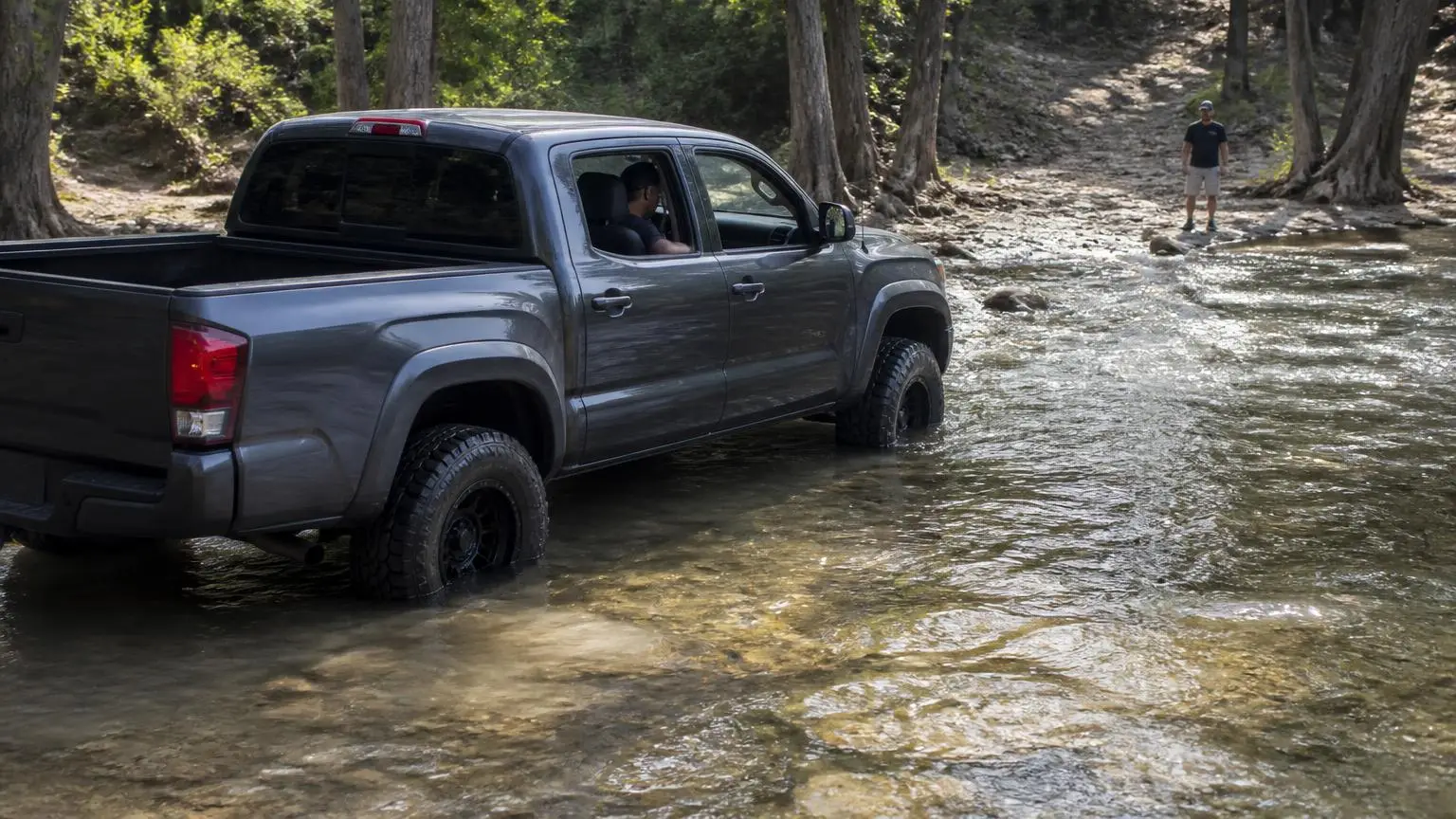 Lifted pickup splashing slowly through a shallow creek