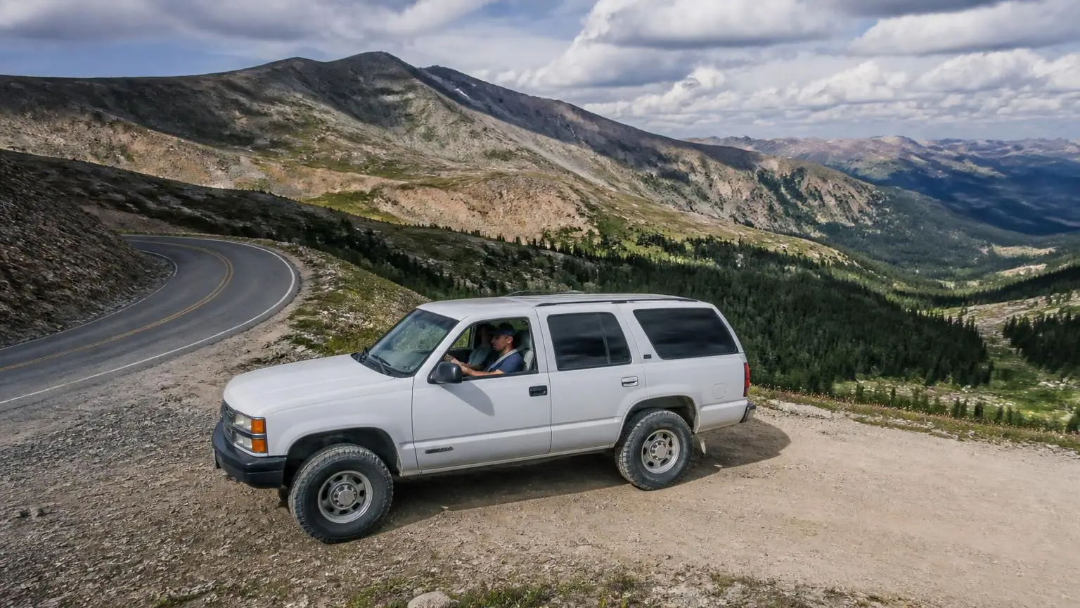 SUV transitioning from a paved pass to a dirt road above treeline