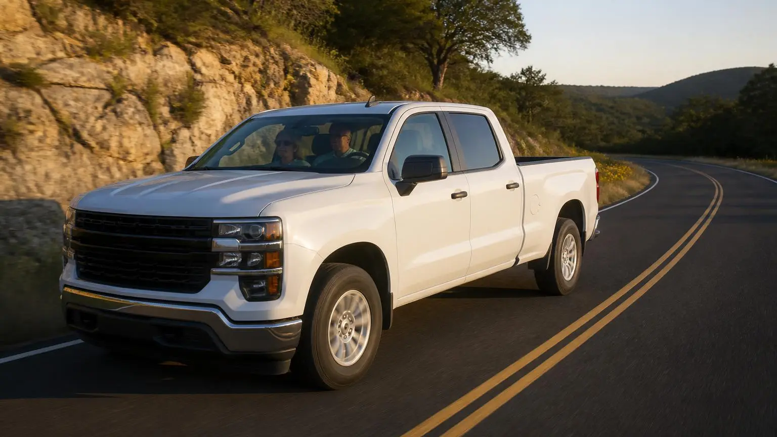 White full-size pickup cruising a two-lane road through rolling hill country at golden hour