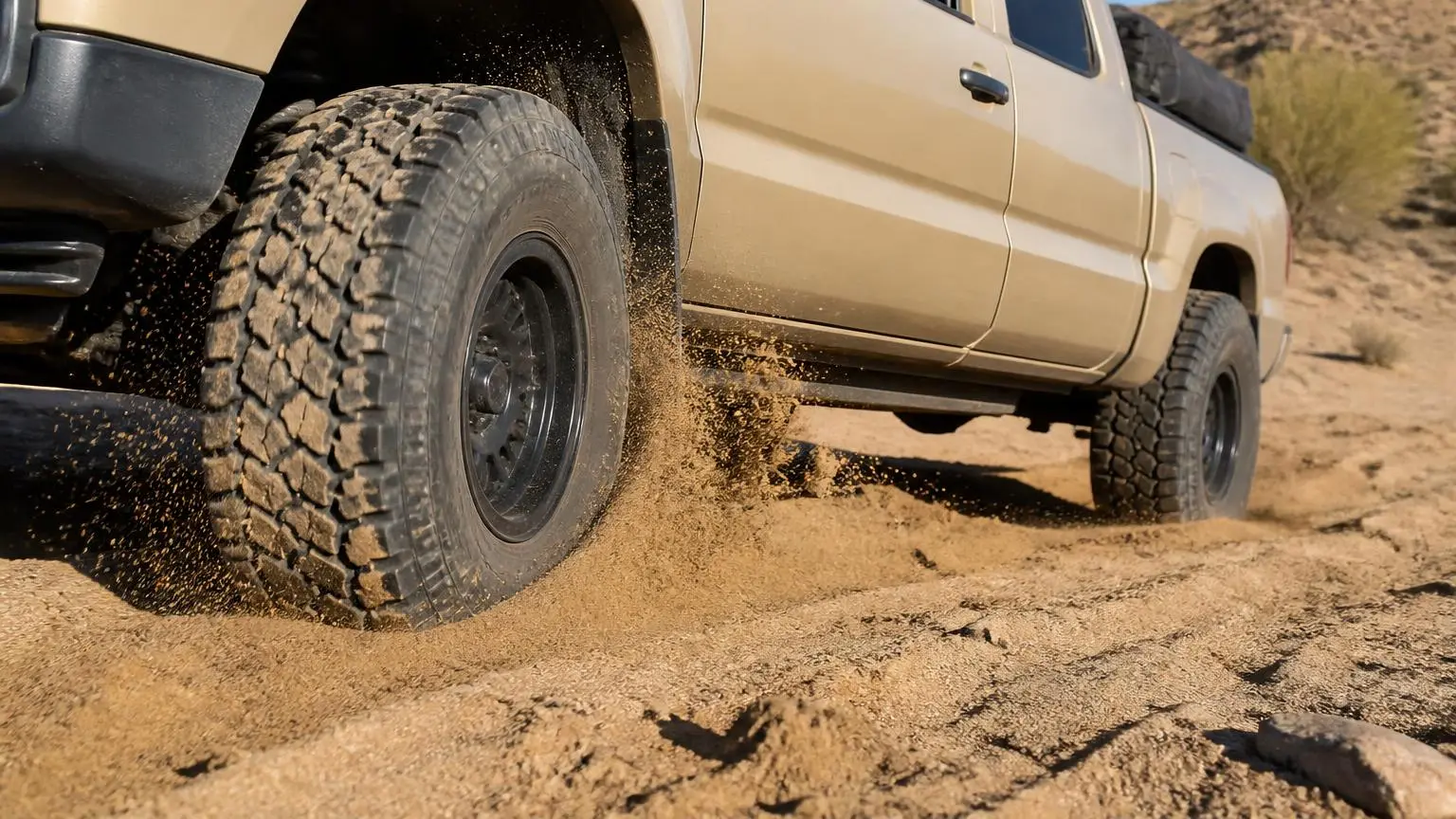 Close low shot of an all-terrain tire churning through a desert wash